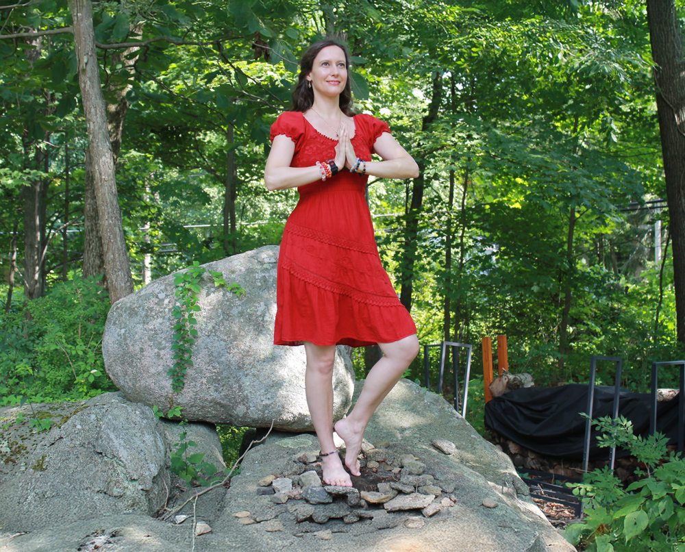 Milena in a circle of rocks wearing a red dress holding her hands in prayer by her heart